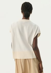 Strik uden ærmer i creme med lyseblå striber, der har en ribbekant og en afslappet pasform. Blød tekstur, minimalistisk design.