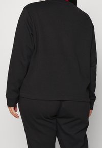 Sudadera negra con un diseño simple, cuello redondo y puños acanalados. Tejido suave con un corte relajado, combinada con pantalones a juego.