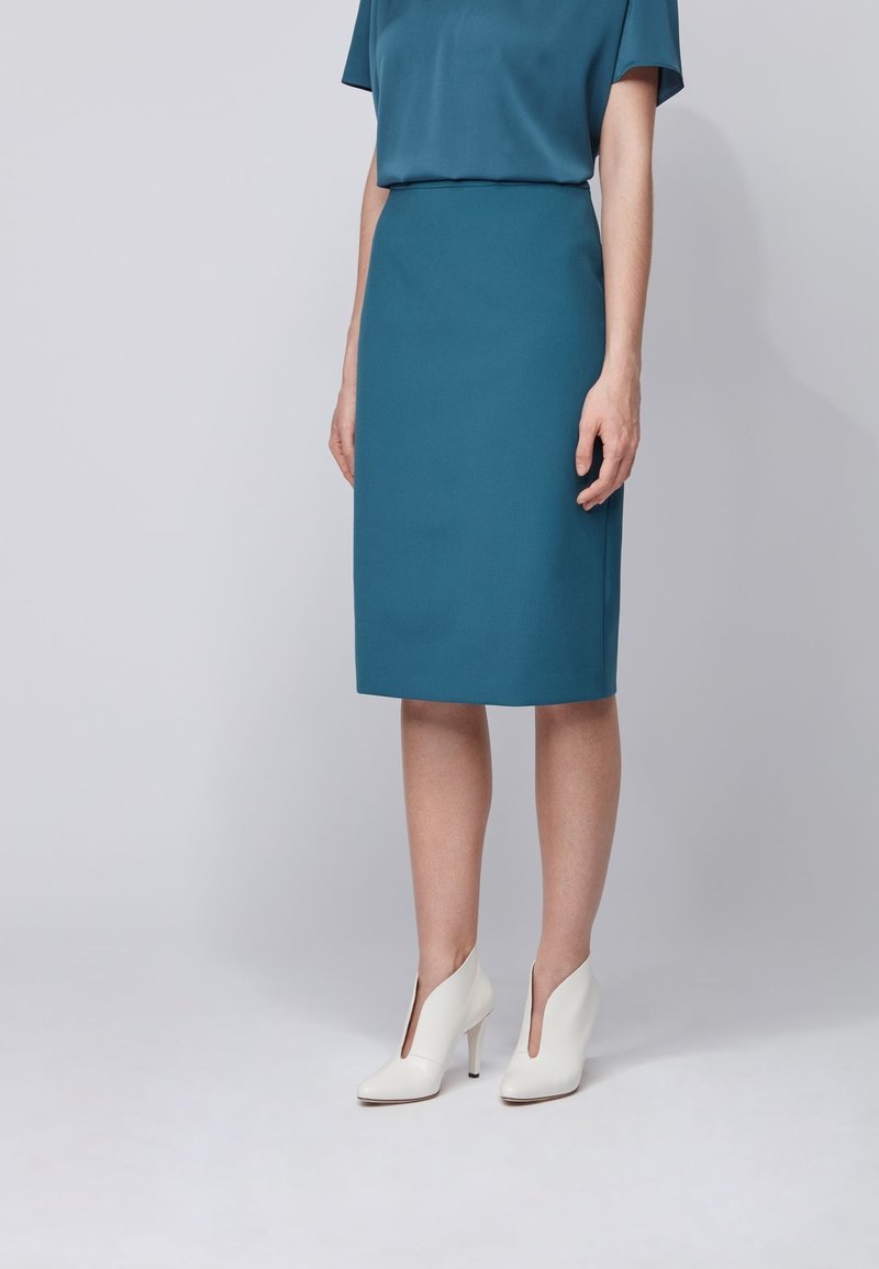 Turkos blyertskjol i matchande blus med en slät textur. Bärs med vita ankelstövlar med sidoklipp.