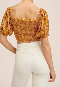 Crop top floral jaune avec des manches bouffantes et un décolleté carré ; associé à un jean blanc taille haute. Tissu doux et accents froncés.