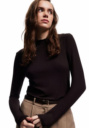 Haut noir à manches longues côtelé avec un col montant, silhouette ajustée et tissu texturé. Associé à un pantalon beige taille haute et une ceinture.