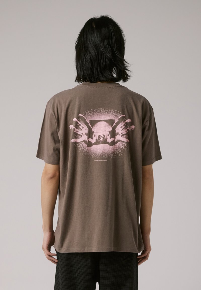 Brown cotton t-shirt featuring a graphic design of two pink hands in front of a faded image. Loose fit with a crew neckline.