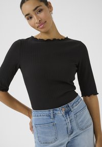 Sort ribbet top med korte, bølgede ærmer parret med lyseblå denim jeans med mid-rise talje og baglommer.