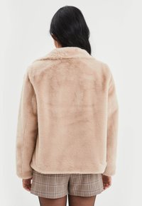 Faux fur jas in zacht beige, met een kraag, losse pasvorm en lange mouwen. De textuur is pluizig, wat de warmte en het comfort vergroot.