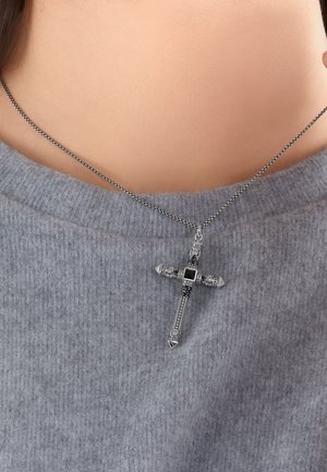 Silberner Kreuzanhänger mit filigranen schwarzen Details an einer Kette, getragen um den Hals über einem grauen, weichen Strickpullover.
