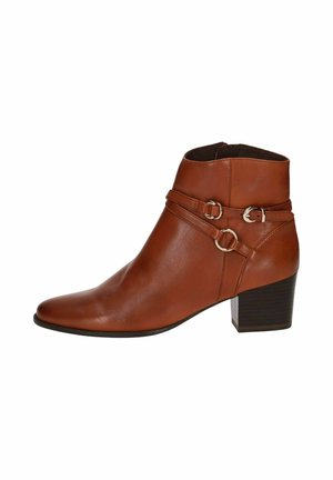 Bota de cuero marrón hasta el tobillo con punta afilada y tacón cuadrado, que presenta dos correas decorativas con acentos metálicos circulares. Textura suave.