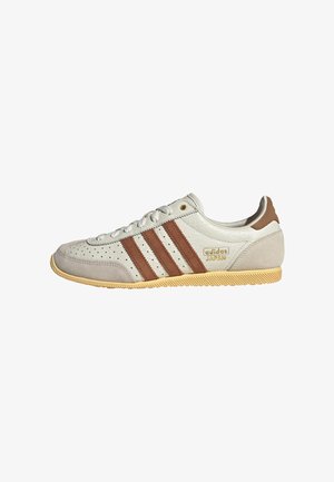 Beżowy sneaker z brązowymi paskami, perforowanymi detalami, wykonany z zamszu i skóry, z gumową podeszwą oraz złotym logo "adidas JAPAN".