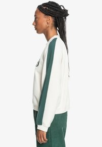 Sudadera de felpa blanca con rayas laterales verdes, cuello redondo, puños acanalados y detalle bordado en el pecho.