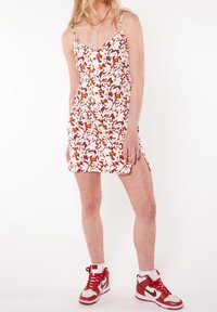 Woman wearing a sleeveless floral mini dress with white, orange, and brown colors, paired with red and white high-top sneakers.