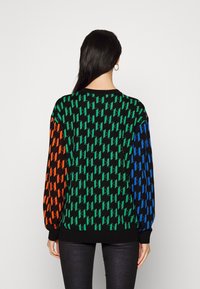 Maglione nero con un motivo ripetuto di forme geometriche verdi, arancioni e blu. Presenta maniche lunghe e un collo rotondo.