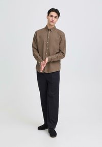 Chemise marron à boutons avec col, manches longues et coupe décontractée, associée à un pantalon foncé et des chaussures noires. Design simple et texturé.