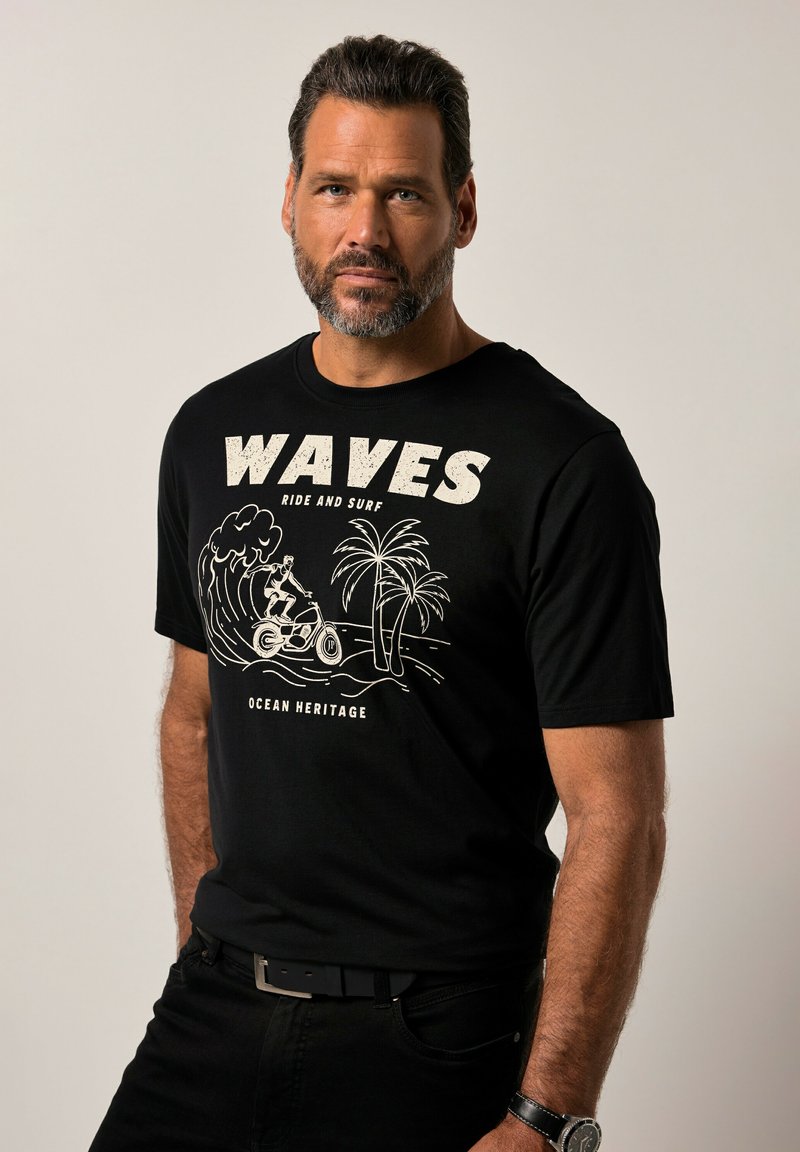 Zwarte katoenen t-shirt met een witte grafische afbeelding van een surfer, golven en palmbomen, met de tekst "WAVES RIDE AND SURF" erboven.