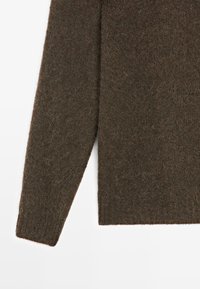 Manica e parte inferiore del torso di un maglione lavorato a maglia di un marrone scuro e morbido su sfondo bianco, che mostra la texture e i dettagli del tessuto.