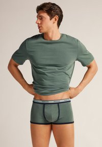 Grön bomull T-shirt med rund halsringning och korta ärmar. Matchas med gröna boxerkalsonger i samma färg med kontrasterande marinblå kant och logotyp.