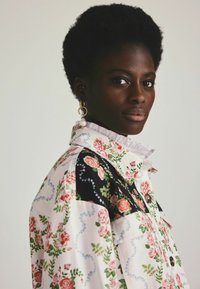 Bloemmotief shirt met een mengsel van lichtroze en zwarte stof. Heeft een knoopsluiting, ruches kraag en een oversized pasvorm.