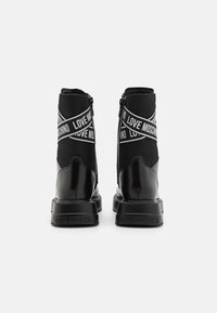 Mustad mustad kingad, mis on valmistatud siledast sünteetilisest materjalist ja kummist tallaga. Omavad külgzipperit ja "LOVE MOSCHINO" letrahmust.