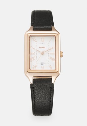 Montre Fossil rectangulaire avec un boîtier en or rose, un cadran blanc, des chiffres romains et un affichage de la date, assortie d'un bracelet en cuir noir texturé.