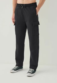 Sorte cargo-sweatpants med elastisk talje og snøre, der har store sidelommer og en afslappet pasform. Bærer grønne sneakers.
