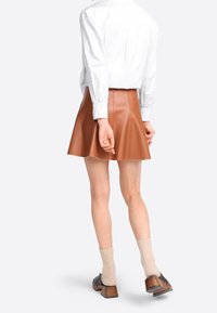 Gonna mini in pelle marrone con pieghe verticali, indossata con una camicia bianca. Completata da calzini a coste beige e zoccoli scuri con tacco in legno.