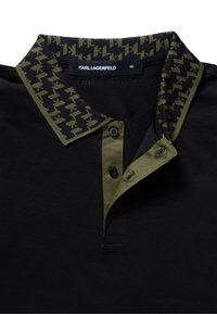 Černé polotričko s kontrastním límcem se vzorem v zelené a černé barvě, se třemi černými knoflíky a detaily na límci.