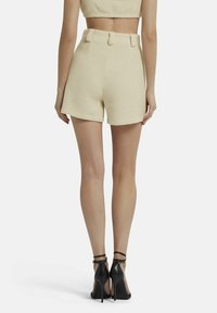 Hoge taille crèmekleurige shorts van textuurstof, met zijzakken, ceintuurlussen en een rechte zoom, gecombineerd met zwarte stilettohakken.