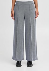 Pantalon gris à jambes larges en tissu doux à la texture lisse avec des plis, associé à des bottines noires.