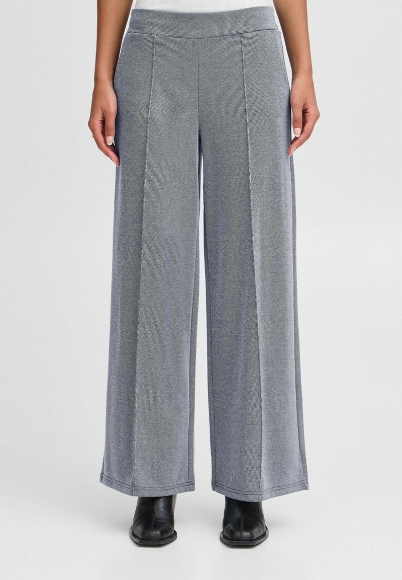 Pantalon gris à jambes larges en tissu doux à la texture lisse avec des plis, associé à des bottines noires.