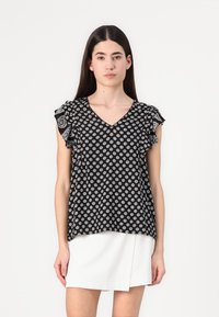 Blusa nera con motivo floreale bianco, scollo a V e maniche corte con volant. Il tessuto sembra leggero e texture.