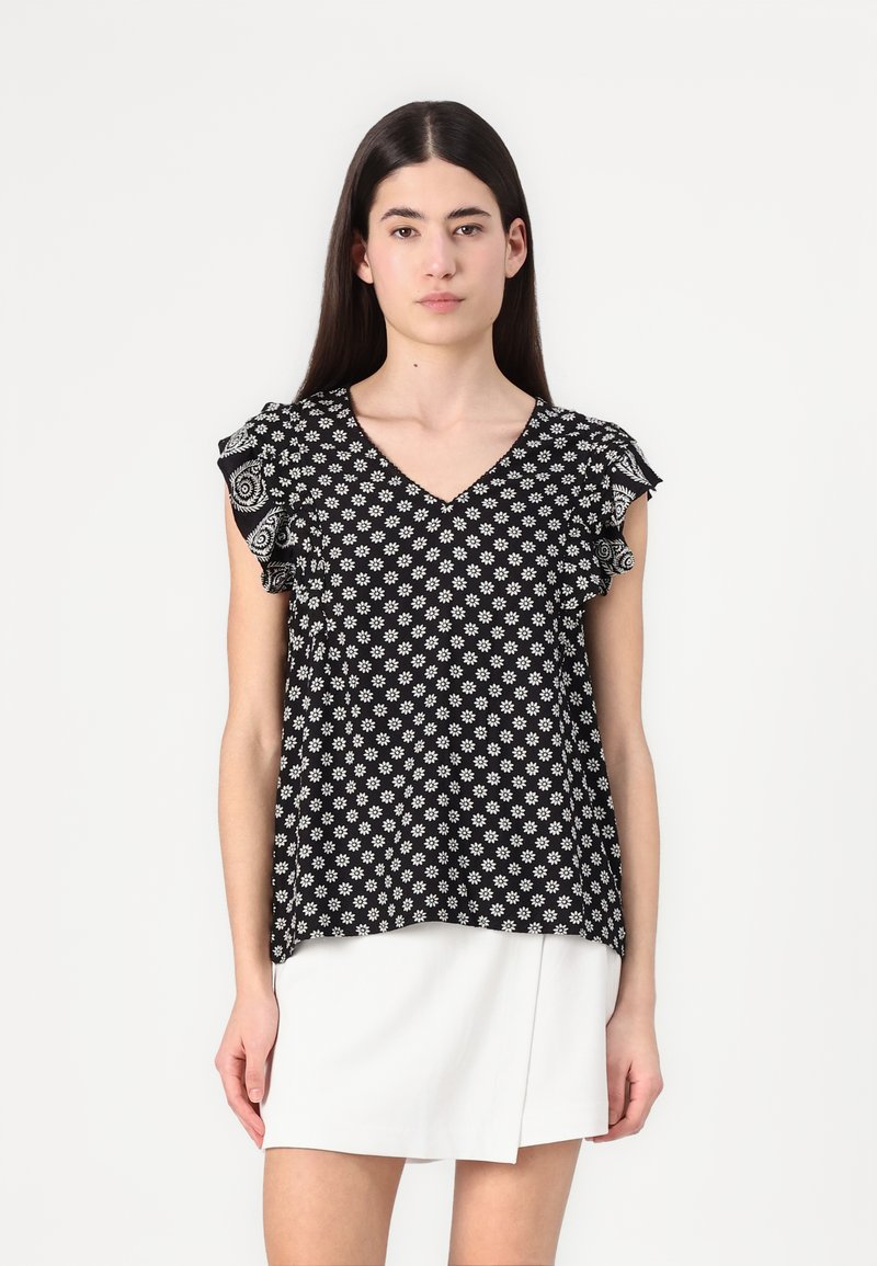 Blusa nera con motivo floreale bianco, scollo a V e maniche corte con volant. Il tessuto sembra leggero e texture.