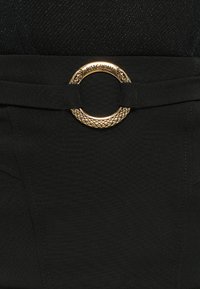 Zwarte riem met een ronde gouden gesp met een slangenstructuur ontwerp en logo. De riem is gemaakt van een gladde stof met gestructureerde details.