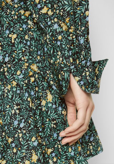 Vestido floral com fundo preto, apresentando folhas verdes, flores amarelas e azuis. Os detalhes incluem tecido franzido e punhos largos.