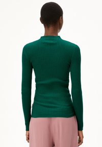 Groene geribde langemouwen top met een hoge halslijn, met een aansluitende pasvorm en textuurstof, gecombineerd met lichtroze broeken.