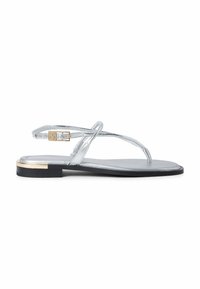 Silver flat sandal with thin straps, ankle buckle, and a small gold accent on the heel, shown on a white background.