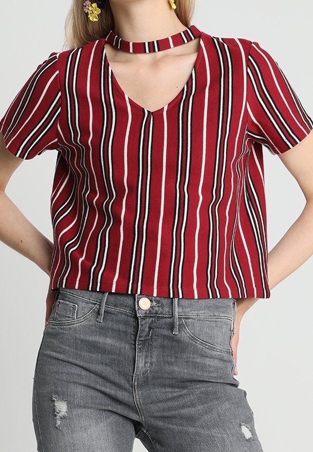 Top de manga corta a rayas rojas y negras con escote en V y detalle de gargantilla, que presenta un corte holgado y un tejido texturizado. Combinado con unos jeans grises desgastados.