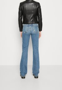 Zwarte leren jas met een getailleerd ontwerp, gecombineerd met blauwe uitlopende jeans met een klassieke vijfzakkenstijl en subtiele slijtageplekken.