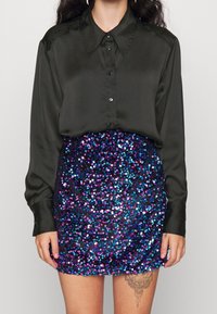 Černá saténová košile s knoflíky a límečkem, která je spárována s mini sukní zdobenou flitry v mnohobarevných modro-fialovo-růžových vzorech.