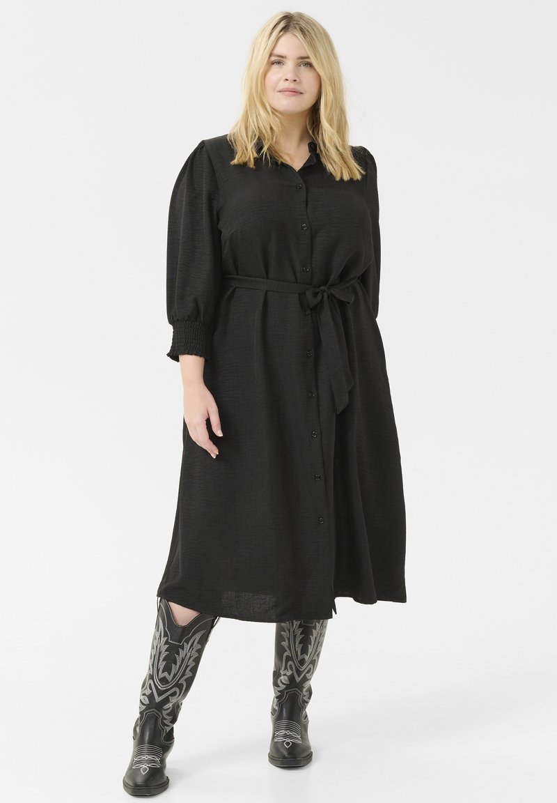 Black midi dress with button detail, belt at waist, and puffed sleeves. Paired with black cowboy boots featuring white floral embroidery.