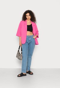 Blazer oversized rosa brilhante, top cropped preto, jeans reto azul claro, sandálias slide pretas e uma bolsa com padrão zebra.