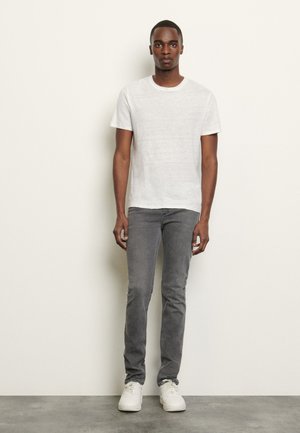 Weißes T-Shirt mit kurzen Ärmeln, graue Slim-Fit-Jeans und weiße Sneaker. Glatter Stoff mit klassischem Rundhalsausschnitt und subtiler Textur.