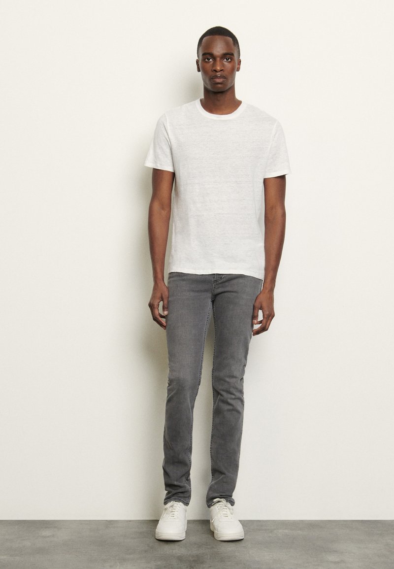 Hvit kortermet t-skjorte, grå slim-fit jeans og hvite joggesko. Glatt stoff med klassisk rund hals og subtil tekstur.