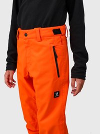 Person iført klare orange bukser med sort lynlås-lomme og sort logo-patch, parret med en sort langærmet top, stående.