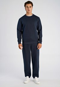 Marineblauwe sweatshirts en bijpassende joggingbroeken gemaakt van zachte stof, met een ronde hals en geribbelde manchetten, gecombineerd met witte sneakers.