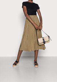 Khaki plisowana spódnica, czarna dopasowana koszulka, czarne sandały i pleciona torebka z czarnymi akcentami. Gładki materiał i rozszerzany kształt podkreślają swobodny styl.