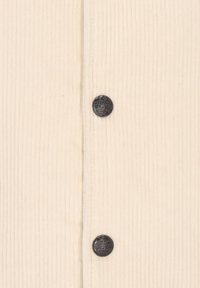 Ivory corduroy fabric with vertical ribbing, featuring two metallic buttons and a subtle texture.