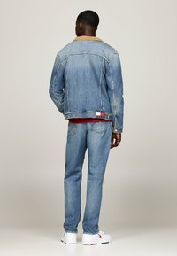 Chaqueta de mezclilla azul claro con un collar de pana, llevada sobre una camiseta roja y jeans claros. Las zapatillas blancas tienen un acento de logo.