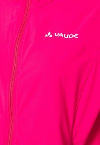 Veste zippée rose avec logo Vaude blanc sur la poitrine, montrant la fermeture éclair avant et une partie de la manche.