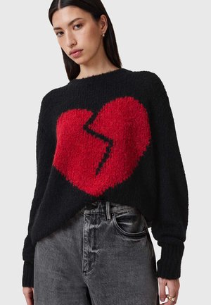 Zwart gebreid trui met een grote rode gebroken hartgrafiek. Losse pasvorm met geribbelde manchetten en een zachte, textuurachtige afwerking. Gecombineerd met vervaagde grijze jeans.