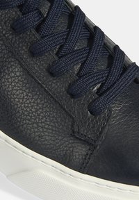 Marineblaue Leder-Sneaker mit strukturiertem Obermaterial, passender Schnürung und einer weißen Gummisohle. Eine Nahaufnahme hebt die Material- und Nähdetails hervor.
