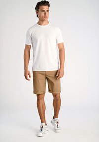 T-shirt blanche à manches courtes, shorts à carreaux kaki retroussés au bas et chaussures de sport grises avec des lacets colorés. Ajustement simple et moderne.