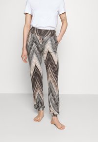 Vzorce hlače zzožene oblike z zigzag vzorcem v rjavi, smetani in črni barvi. Imajo elastičen pas in manšete na gležnjih, narejene so iz lahkega blaga.